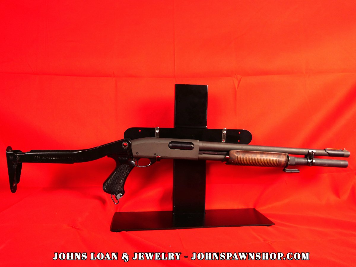 The Remington 870 Magnum police enforcement shotgun from John's Loan & Jewelry, displaying its folding stock, parkerized finish, and tactical configuration against a red backdrop.