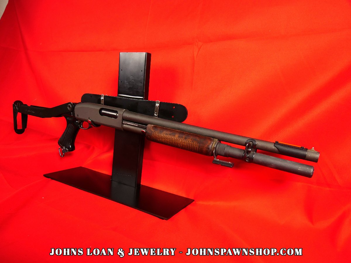 Profile view of the Remington 870 Magnum police shotgun, exhibiting the folding stock, pistol grip, and 12-gauge chamber, offered by John's Loan & Jewelry.