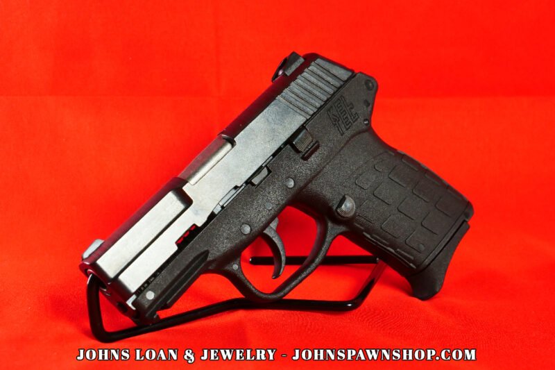 Angled studio shot of a black KelTec PF-9 semi-auto pistol, with a light gray slide, displayed on a table at John's Loan & Jewelry, ideal for concealed carry.