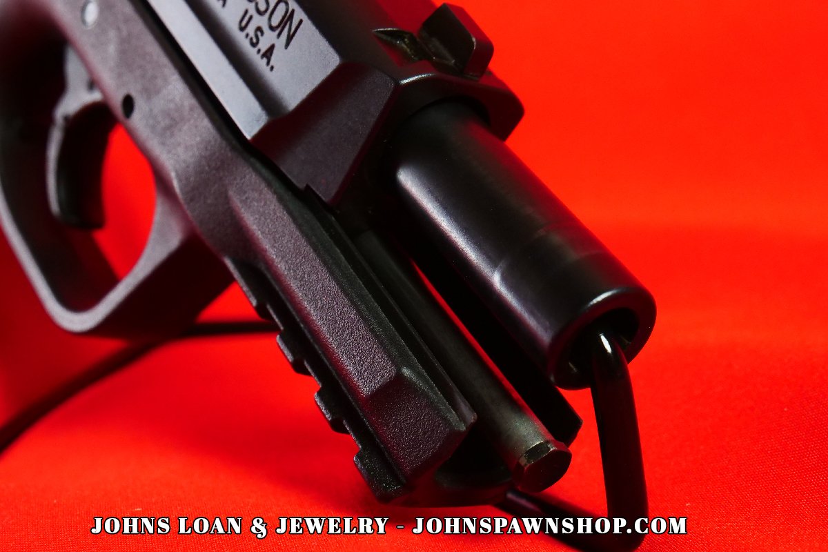 Close-up detail of the Smith & Wesson M&P 9mm pistol's muzzle, showcasing the textured polymer frame and slide. Find police and military firearms at John's Loan & Jewelry.