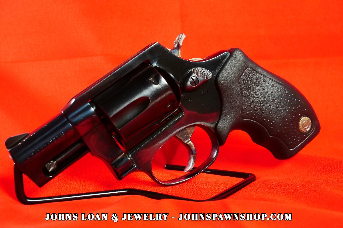 Slightly elevated angle of a Taurus Model 85 snub nose revolver, a five shot .38 Special firearm, on a display stand from John's Loan & Jewelry.