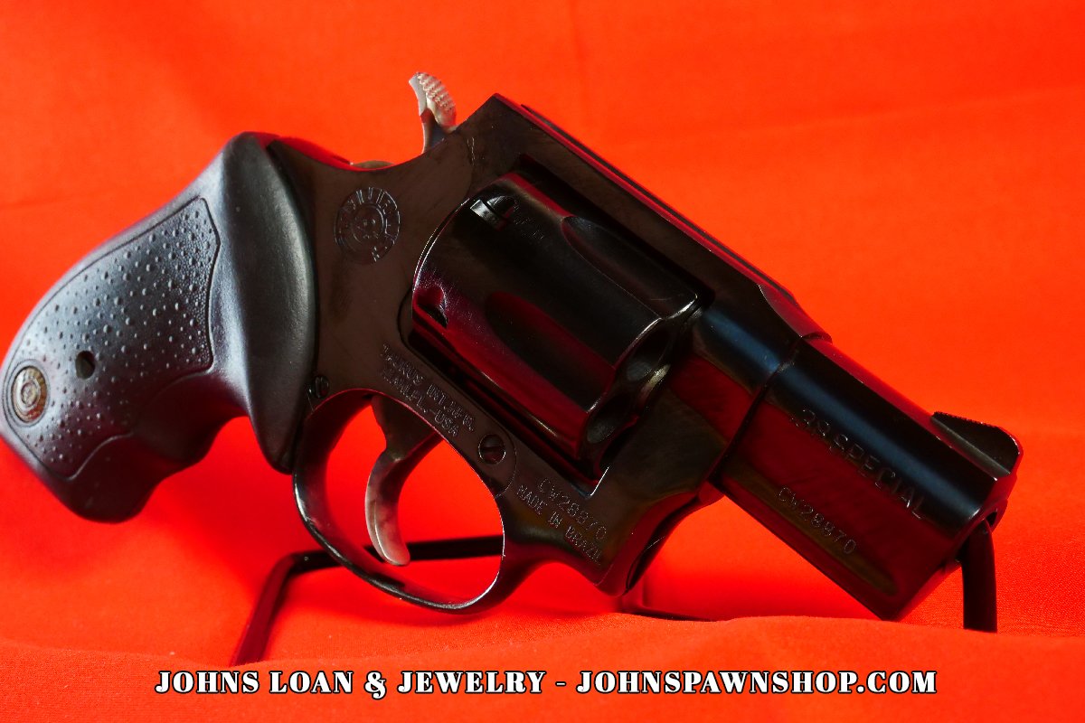 Angled view of a black Taurus Model 85 snub nose revolver, a five shot .38 Special firearm, displayed on a stand and sold by John's Loan & Jewelry.