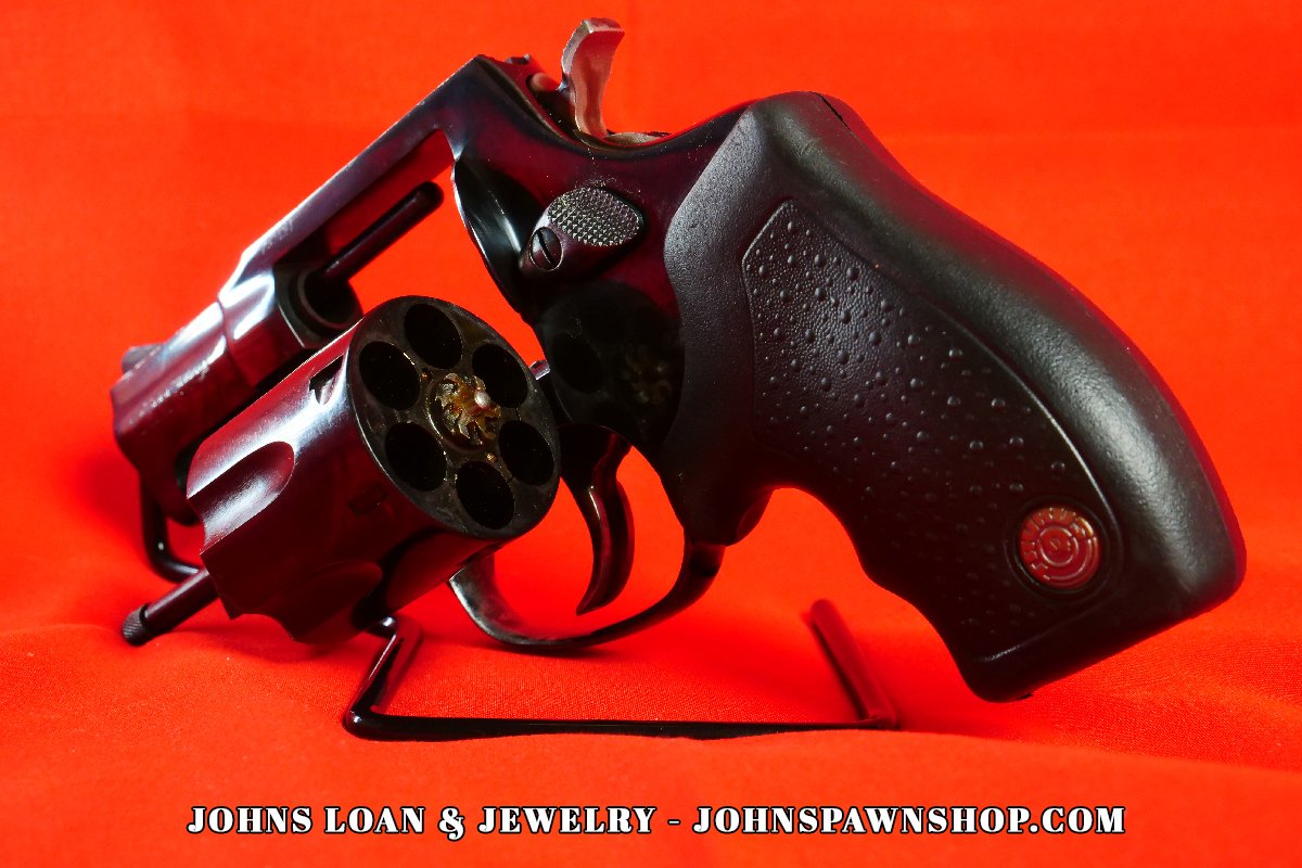 Oblique angle showing the open cylinder of a black Taurus Model 85 five shot revolver in .38 Special on a table, available at John's Loan & Jewelry.