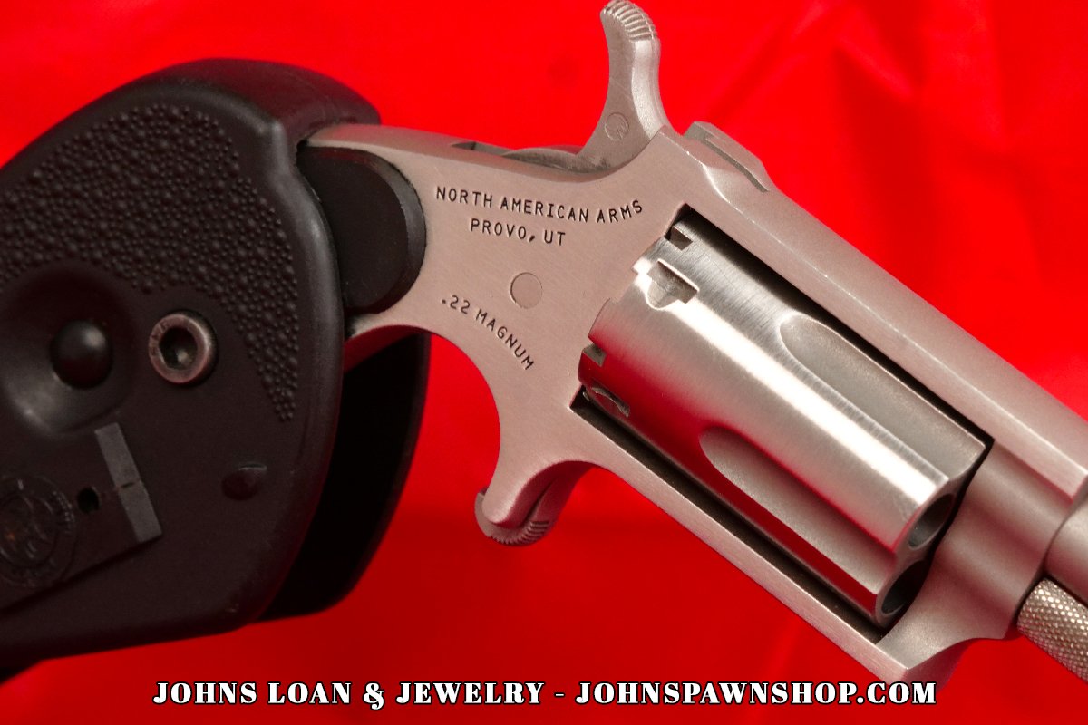 Close-up detail of the North American Arms .22 Magnum revolver offered by John's Loan & Jewelry, showing the stainless steel cylinder, frame markings, and the textured surface of the attached holster grip.