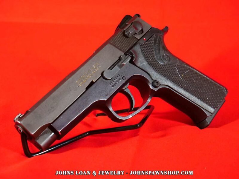 Angled view of a Smith & Wesson Model 910 semi-auto pistol. Features a matte black frame, stainless steel slide, and textured grips. Available at John's Loan & Jewelry.